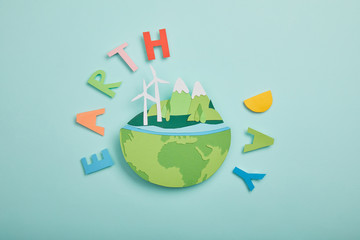 top view of paper cut planet with renewable energy sources and colorful paper letters on turquoise background, earth day concept