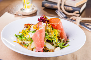 Close up Green Salad with prosciutto and pears in white plate close up. Served restaurant table. Selective focus, copy space.