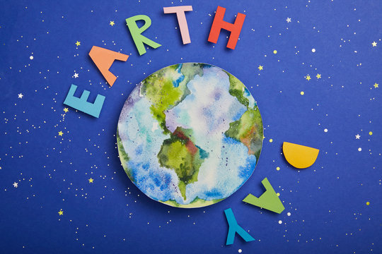 top view of colorful paper letters and planet picture on violet background with stars, earth day concept