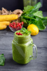 Healthy green spinach smoothie in a jar mug decorated with mint and red currant berries with ingridients on the black wooden table. Selective focus. Detox concept.