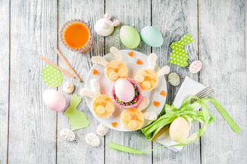 Easter kids food creative ideas, breakfast sandwiches  in form of bunny rabbits, with colorful eggs, carrot juice and decorations, wooden background copy space