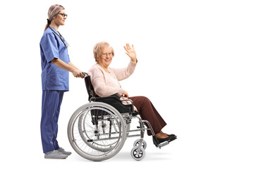 Nurse pushing a senior woman in a wheelchair waving