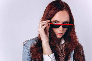 Naklejka premium Portrait of young fashion gorgeous caucasian hipster girl with red headed hairstyle on white background in sun glasses. Beauty, commercial concept