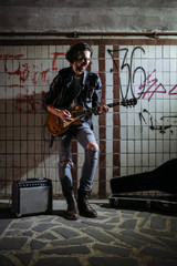 A street musician playing on guitar in the underpass. Vagrant lifestyle. Playing in the underpass to make a living. Unemployed musician. Future rock star.