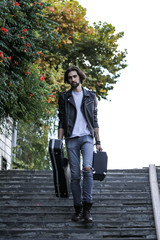 Street musician holding a case with a guitar and amplifier. Goes down the stairs to the underground passage. Vagrant lifestyle. Playing to make money a living. Unemployed musician. Future rock star.