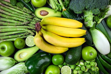 Raw healthy food clean eating vegetables and fruits asparagus, broccoli, avocado, banana, brussels, cucumber, pepper, celery, apple, lime, spinach and chicory on dark stone background, top view