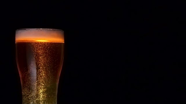 Medium shot stream of glass bocal of beer with many air bubbles rising up isolated at black background slow motion