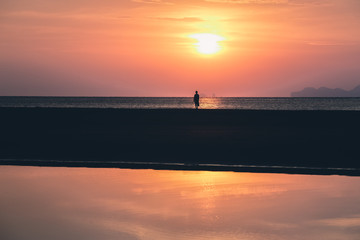 Fototapeta premium Women’s is lonely on the beach at sunset. Beautiful sky and clouds with reflection on water. She’s travel in summer holiday