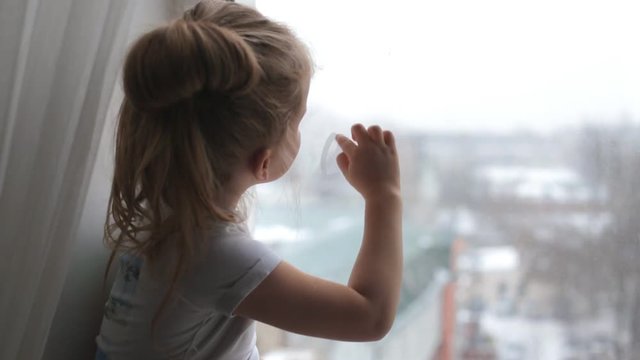 Little girl draws a finger on the window hearts