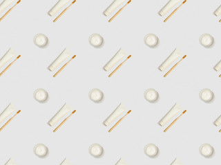 diagonally located bamboo toothbrushes, toothpaste in tubes and cosmetic cream on grey background, seamless background pattern