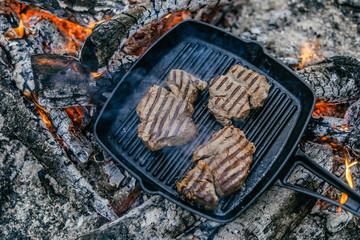 campfire red meat in pan, near the fire outdoors. bushcraft, adventure, travel, tourism and camping concept