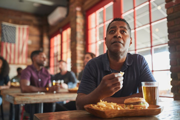 Man Watching Game On Screen In Sports Bar Eating Burger And Fries