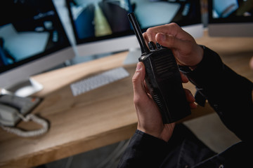 cropped view of guard holding walkie-talkie at workspace - obrazy, fototapety, plakaty