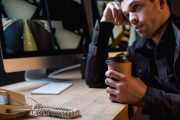 tired guard holding paper cup and looking at computer monitor