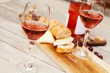 Naklejka premium Two glasses of rose wine and board with fruits, bread and cheese on wooden table