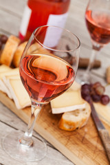 Two glasses of rose wine and board with fruits, bread and cheese on wooden table