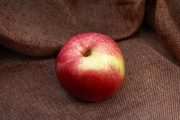 An Apple in drops of water lies on a bronze-brown burlap.