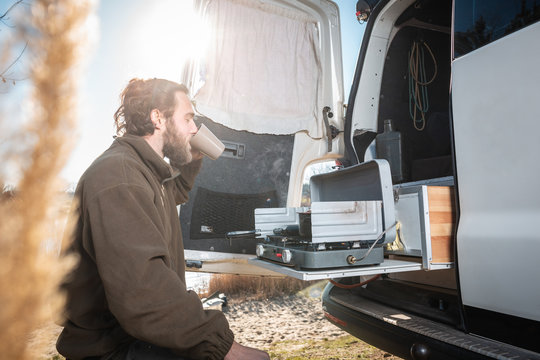 Mann sitzt am Camper-Van und genießt eine Tasse Kaffee