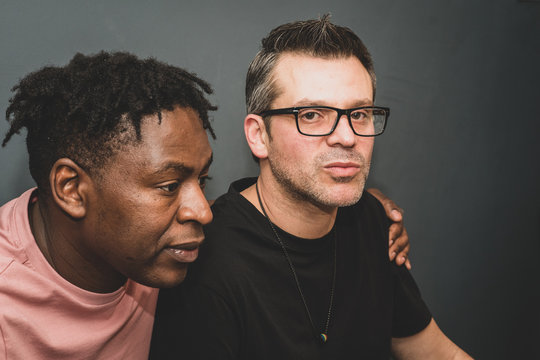 An interracial gay couple pose before the camera to have their pictures taken - black man and mixed race man with stubble - on a black background - with copy space.