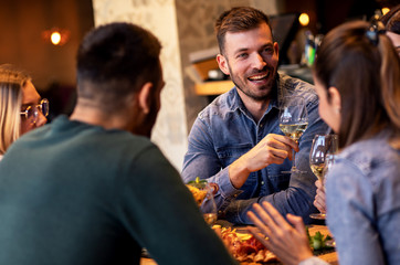 Group of young friends having fun in restaurant, talking and laughing while toasting with glass of wine.
