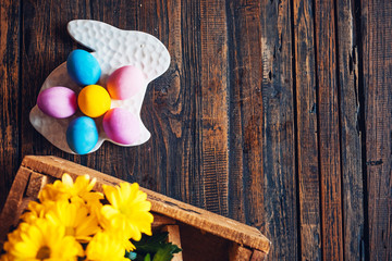 Easter eggs on a ceramic stand, with blooming twigs of willow and yellow chamomile chrysanthemum flowers on a rural wooden table. Hello spring and easter concept