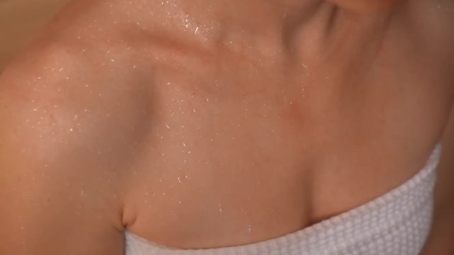 Close-up drops of sweat flowing on sexy female naked body during enjoying spa sauna. Attractive young European woman chest wrapped towel taking bath house high angle