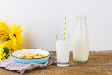 A glass of milk with milk bottle and cookies on wooden table