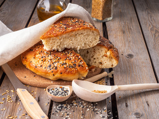 Home-made bread in a slit and a large chunk of sliced bread on a rustic board table, near wooden spoons with seeds