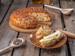 Home-made bread in a cut and a slice of sliced bread smeared with butter on a rustic wooden board table, next to wooden spoons with flax and sesame seeds.