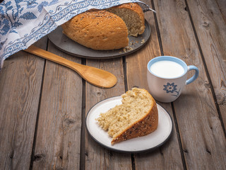 A slice of homemade bread on a light plate, a mug of milk, in the background bread with a slit