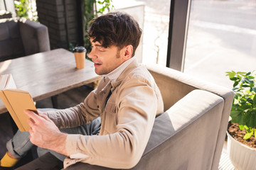 handsome man smiling while reading book in cafe