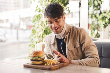happy man looking at french fries near delicious burger on cutting board in cafe
