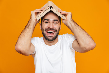 Image of optimistic man 30s in white t-shirt holding a book on his head, isolated over yellow...