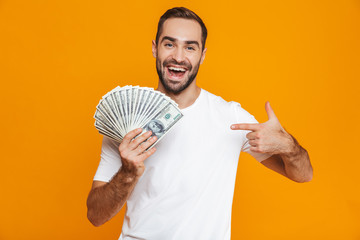 Photo of unshaved man 30s in casual wear holding bunch of money, isolated over yellow background