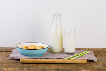 A glass of milk with milk bottle and cookies on wooden table