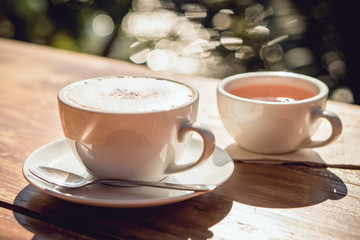 Hot coffee and hot tea place on the wooden table in early morning with copyspace, white cup and silver spoon.