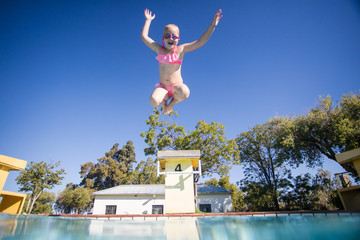 Wide angle view as a young girl jumps into a swimming pool