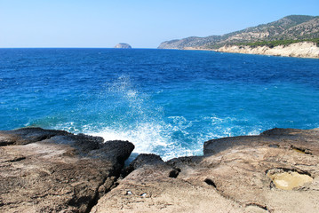 Large stones washed by sea waves with white foam against a blue sky, Cape Fourny, Rhodes Island, Greece