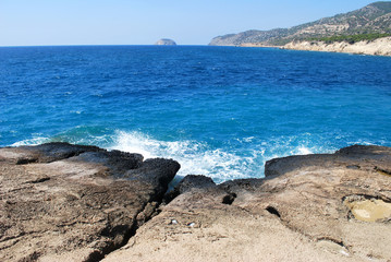 Large stones washed by sea waves with white foam against a blue sky, Cape Fourny, Rhodes Island, Greece