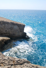 Close-up of large stones washed by sea waves with white foam against a blue sky, Cape Fourni, Rhodes Island, Greece