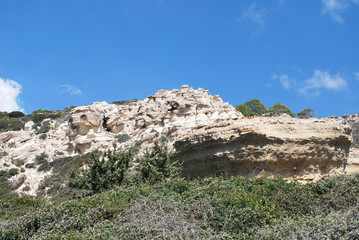 Fototapeta na wymiar Large white stones among green plants against the blue sky, Cape Fourny, Rhodes Island, Greece