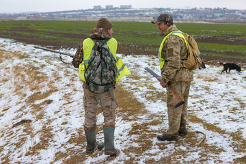 Fototapeta premium Hunter with a gun and a dog go on the first snow in the steppe, Hunting pheasant in a reflective vest 