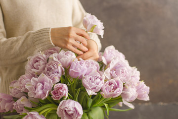 Florist at work: pretty young woman making a big bouquet of double violet tulip flowers on a dark rustik background