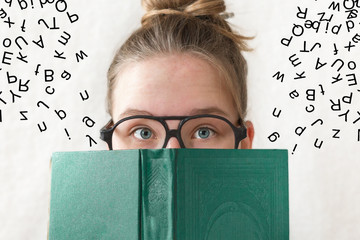 Girl teen in glasses reading a book and letters, joke, humor fly out of it. The idea of learning,...