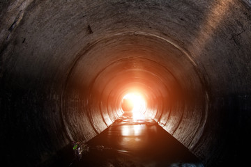 Round underground urban sewer tunnel with dirty sewage water. A light in the end of a tunnel