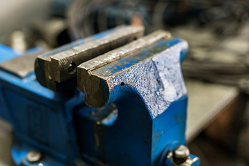 Blue old vise mounted on a workbench in a workshop or carpentry shop. Device for clamping and holding objects and parts.