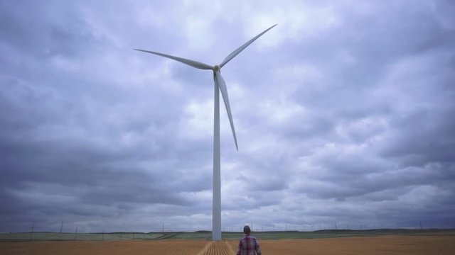 Man on field walking toward large wind turbine near Fort Macleod, Alberta, Canada