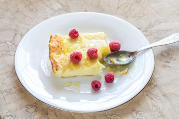 Piece of curd casserole with raspberries and honey on white plate with spoon on wooden cut. 