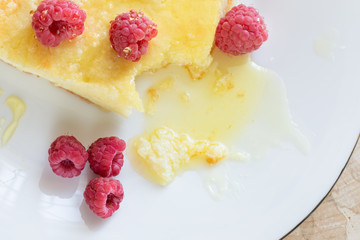 Close-up cheese casserole with raspberries drizzled with honey on white plate. 
