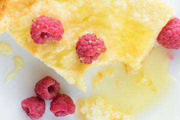 Close-up piece of traditional curd casserole with raspberries and honey on white plate.